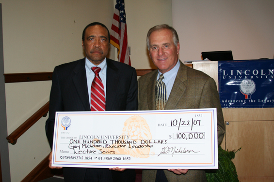 Michael Hill (left), vice president for development and external relations, accepts mock  check from donor and alumnus Gary Michelson